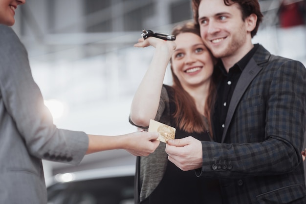 Orgullosos dueños. Hermosa joven pareja feliz abrazando de pie cerca de su auto recién comprado sonriendo alegremente mostrando las llaves del auto a la cámara