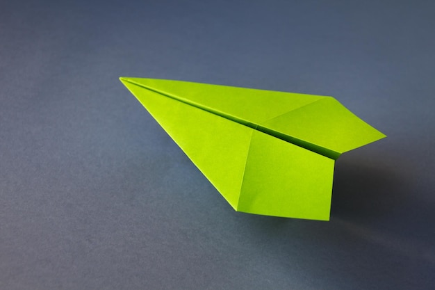 Origami de avión de papel verde aislado sobre un fondo gris