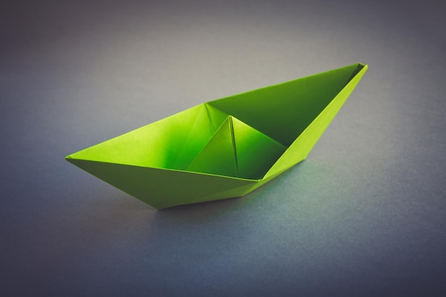 Origami de barco de papel verde aislado sobre un fondo gris