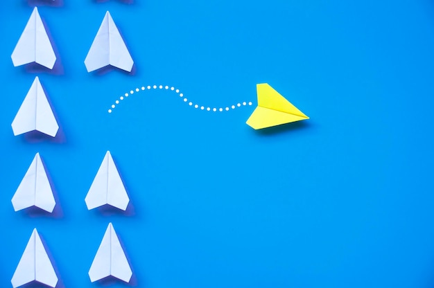 Origami de avião de papel amarelo deixando outros aviões brancos em fundo azul com espaço personalizável para texto ou ideias Conceito de habilidades de liderança e espaço para cópia