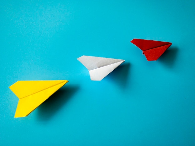 Origami de avião de papel vermelho levando aviões brancos e amarelos sobre fundo azul com espaço personalizável para texto Conceito de habilidades de liderança