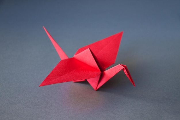 Origami de grulla de papel rojo aislado en un fondo gris