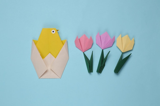 Origami-Huhn und Tulpen auf blauem Hintergrund Frühlings-Ostern-Konzept