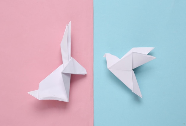 Origami-Kaninchen und Taube auf einem blaurosa Pastellhintergrund Draufsicht
