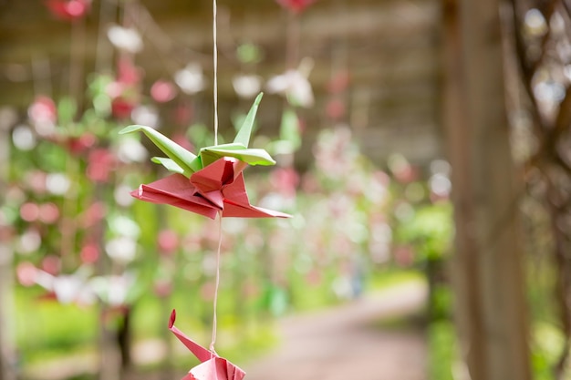 Origami-Kraniche hängen an den Fäden im Garten gegenüber den sonnenbunten Kranichen aus Papier