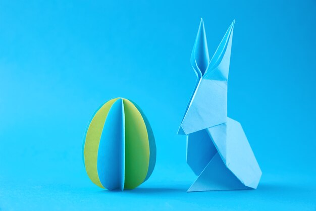 Origami de papel Esater conejo y huevo de color en la pared azul. Concepto de celebración de Pascua