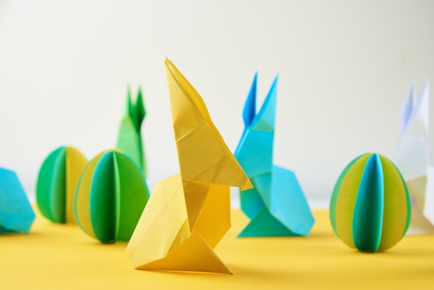 Origami de papel esater conejos y huevos de colores en una pared amarilla concepto de celebración de pascua