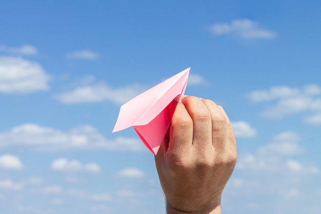 Origami-Papierflugzeug in der jungen männlichen Hand auf blauer bewölkter Himmelsoberfläche