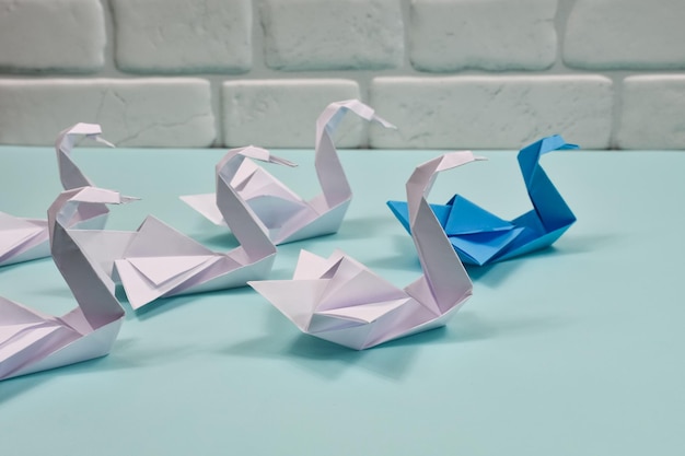 Origami-Papierschwäne auf blauem Hintergrund Führungskonzept Ein blauer Schwan führt einen Schwarm weißer Schwäne an