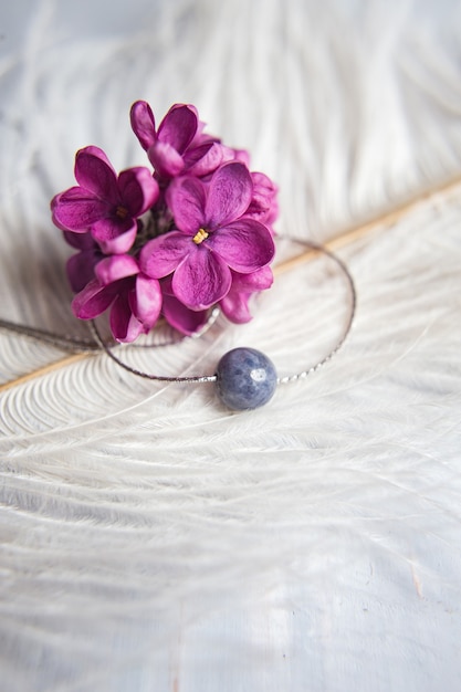 Original collar de bisutería de plata realizado en piedra natural con flores lilas violetas violetas sobre pluma de avestruz blanca. concepto de regalo. accesorios de plata. simulacros de espacio para texto. | Original collar de bisutería de plata realizado en piedra natural con flores lilas violetas violetas sobre pluma de avestruz blanca. concepto de regalo. accesorios de plata. simulacros de espacio para texto. |