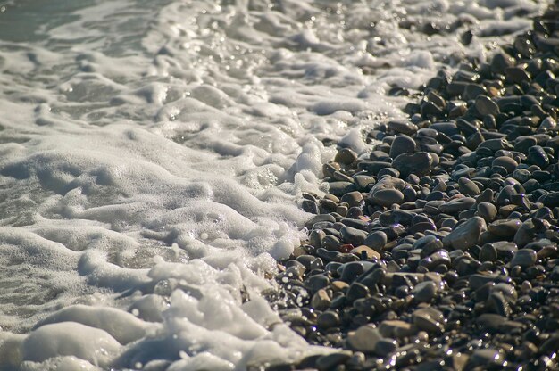 Foto orilla del mar en una playa de guijarros con el agua de las olas rompiendo sobre las rocas mojadas.