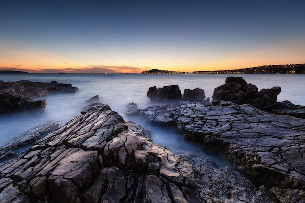 Orilla del mar con rocas al atardecer Paisaje marino en verano Rocas y agua Larga exposición Mar Mediterráneo Imagen de viaje