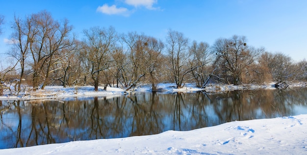 Orilla nevada del pequeño río contra el cielo azul