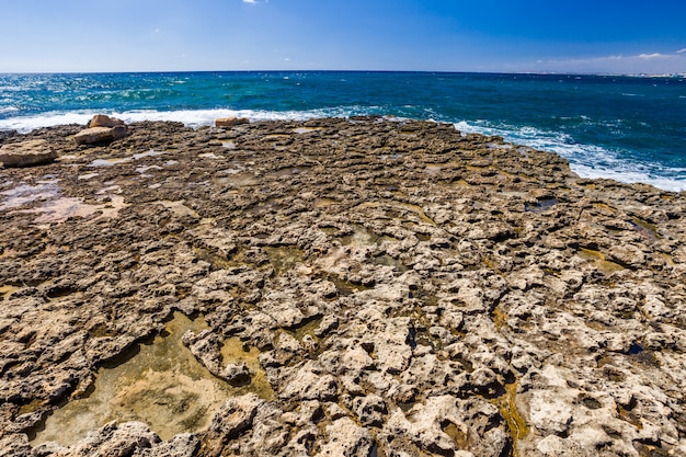 Orilla de piedra rocosa, agua de mar turquesa clara y cielo azul claro día.