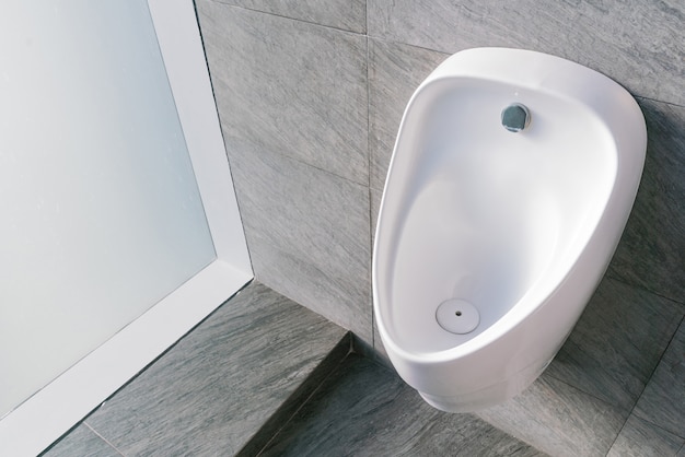 Orinal de cerámica blanca de saneamiento en el baño de hombres con enjuague electrónico higiénico automático que ahorra agua.