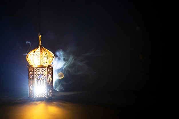 Ornamentelle arabische Laterne mit brennender Kerze, die nachts leuchtet, und glitzernden goldenen Bokeh-Lichtern Feierliche Grußkarte für den muslimischen heiligen Monat Ramadan Kareem