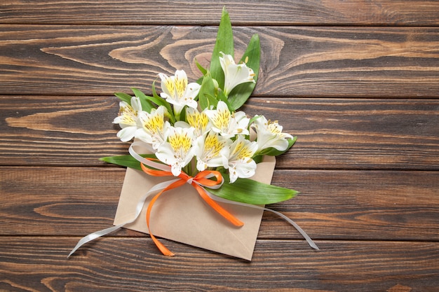 Orquídeas pequenas das flores brancas macias em um envelope esperto do correio em um fundo de madeira