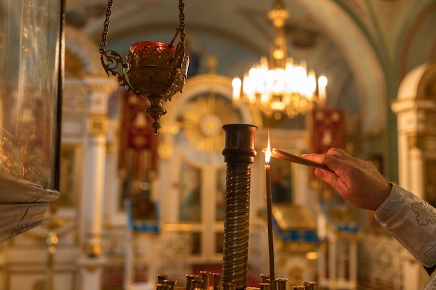 Orthodoxe kirche christentum hand des priesters, der brennende kerzen in der traditionellen orthodoxen kirche anzündet