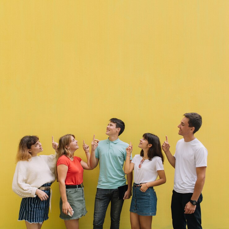 Foto os adolescentes felizes do grupo mostram algo no fundo amarelo do espaço da cópia.