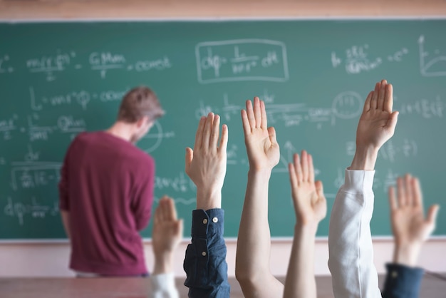 Os alunos da escola com as mãos levantadas em sala de aula aprendendo juntos