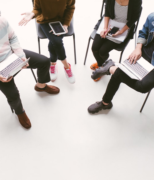 Os alunos sentam-se em um círculo de amigos discutindo entre si com laptop e tablet