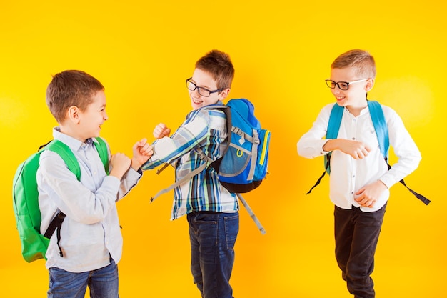 Os alunos sorridentes são facilmente empurrados uns aos outros no fundo amarelo Os meninos com mochilas usam roupas casuais