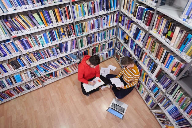 Foto os alunos usam um notebook e uma biblioteca escolar