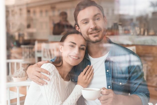 Os amantes bebem café com leite no café acolhedor mulher dá abraço.