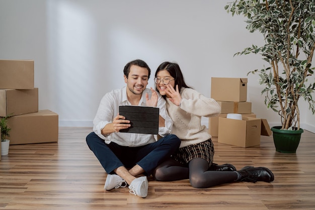 Os amantes estão sentados no chão em um apartamento recém-comprado, um homem elegantemente vestido está segurando um casal de tablet