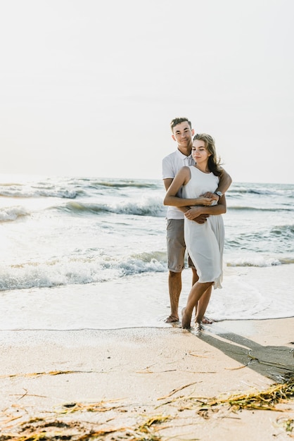 Os amantes perto do oceano se abraçam e se divertem. marido e mulher abraços ao pôr do sol perto do mar. amantes de férias. resto de verão. passeio romântico à beira-mar