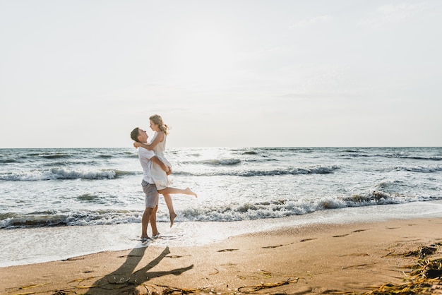 Os amantes perto do oceano se abraçam e se divertem. marido e mulher abraços ao pôr do sol perto do mar. amantes de férias. resto de verão. passeio romântico à beira-mar