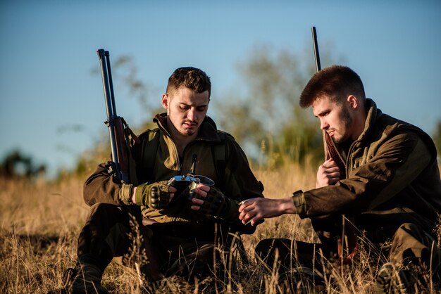 Os amigos dos caçadores desfrutam do lazer. caça com amigos, passatempo de lazer. os caçadores ficam satisfeitos com a captura de bebidas aquecidas. descanse para o conceito de homens reais. caçadores com rifles relaxantes no ambiente natural.