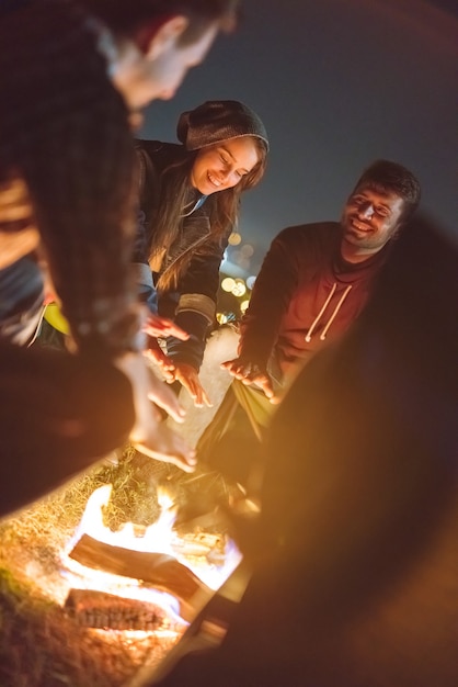 Foto os amigos felizes aquecendo as mãos perto de uma fogueira. noite noite