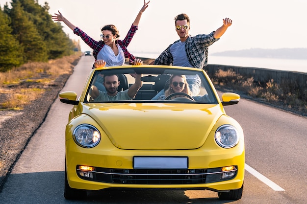 Os amigos felizes estão viajando em um cabriolet amarelo