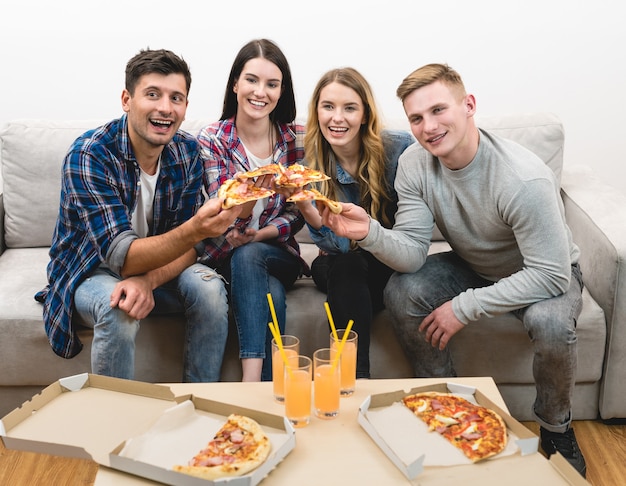 Os amigos felizes no sofá comem pizza no fundo branco