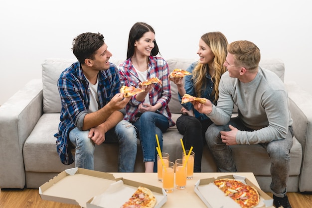 Os amigos felizes no sofá comem pizza no fundo branco