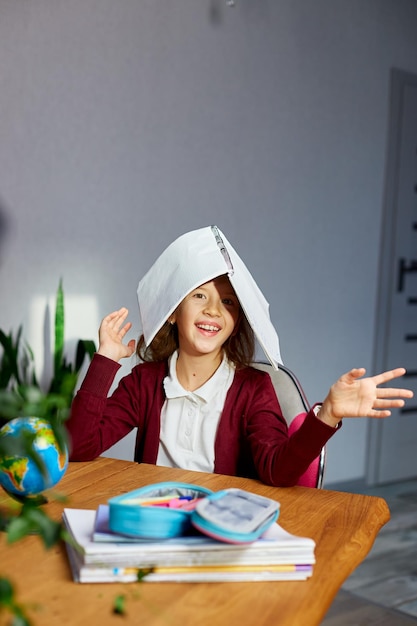 Os braços da menina inteligente da estudante feliz colocam a pasta de trabalho na cabeça