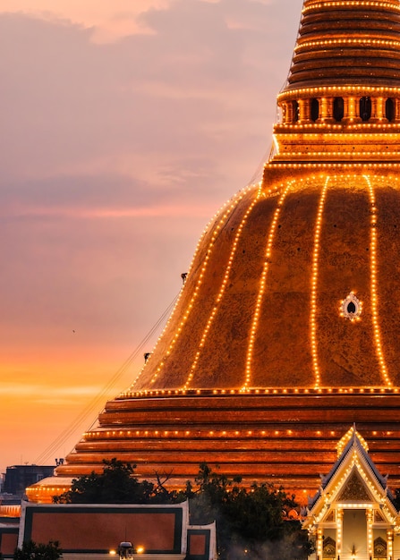 Os budistas subem para decorar com luz a pagoda dourada Phra Pathom Chedi no céu ao pôr do sol no festival anual em Nakhon Pathom