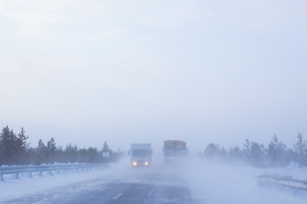 Os carros seguem em uma estrada de inverno com pouca visibilidade, clima e tempestade de neve