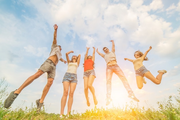 Os cinco amigos felizes pulando no fundo ensolarado