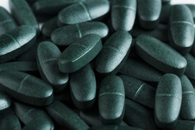 Os comprimidos de espirulina são verdes com multivitaminas em tela inteira como fundo