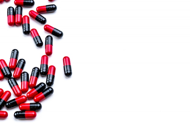 Os comprimidos Vermelho-pretos da cápsula espalharam no fundo branco. Uso de antibióticos com razoável. Indústria farmacêutica. Fundo de farmácia. Saúde global. Pilha de comprimidos da cápsula com espaço de cópia.