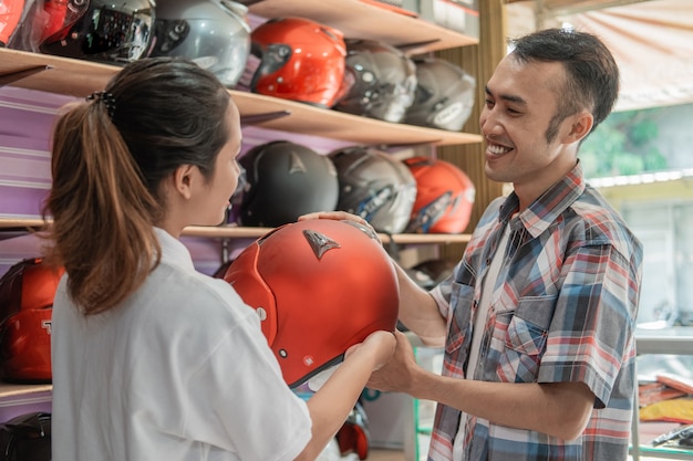 Os consumidores do sexo masculino sorriem ao escolher um capacete servido por uma bela lojista em uma loja de capacetes