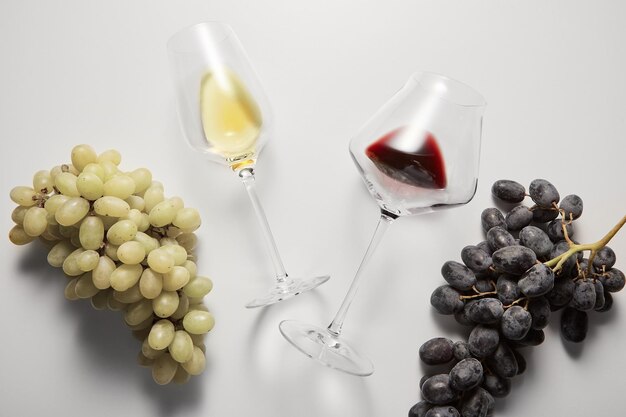 Os copos de vinho com bebidas vermelhas brancas estão entre as uvas