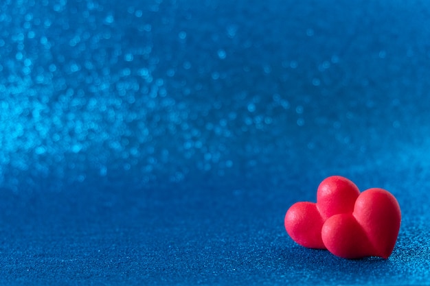 Os corações vermelhos brilhantes abstraem o fundo azul do bokeh. Textura de dia dos namorados.