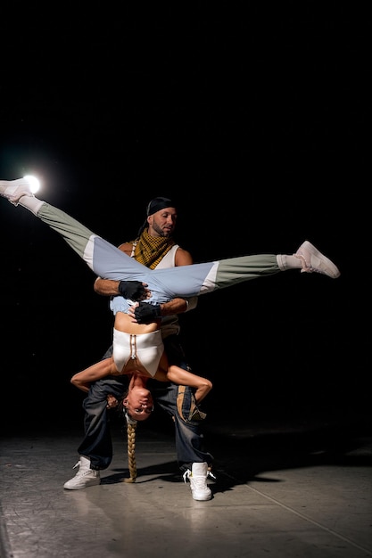 Os dançarinos modernos acolhem a mulher e o homem dançando no preto. Estilo de vida urbano. Geração hip-hop. Performance de dança Hip Hop no palco. Macho e fêmea flexíveis dão desempenho, homem segurando fêmea e levantando