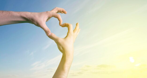 Os dedos das mãos fazem um símbolo da forma do coração contra o céu