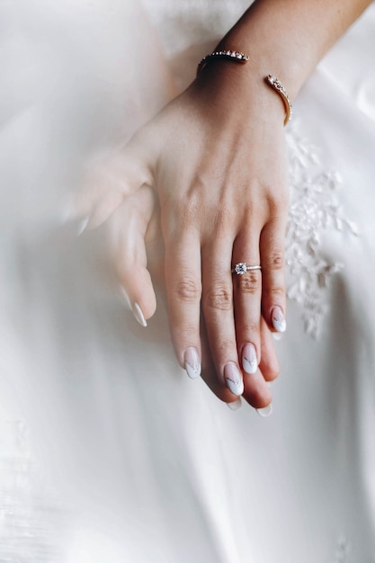 Os dedos macios da noiva com anel de casamento encontram-se no vestido
