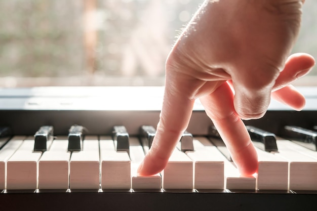 Os dedos pressionam as teclas do piano como se as pernas estivessem andando na luz natural da janela