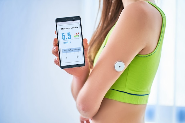 Os diabéticos da mulher controlam e verificam o nível de glicose com um sensor remoto e telefone celular. Monitoramento on-line contínuo dos níveis de glicose sem sangue. Tecnologia médica digital no tratamento da diabetes